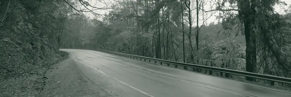 A wet two-lane road curving past a guardrail